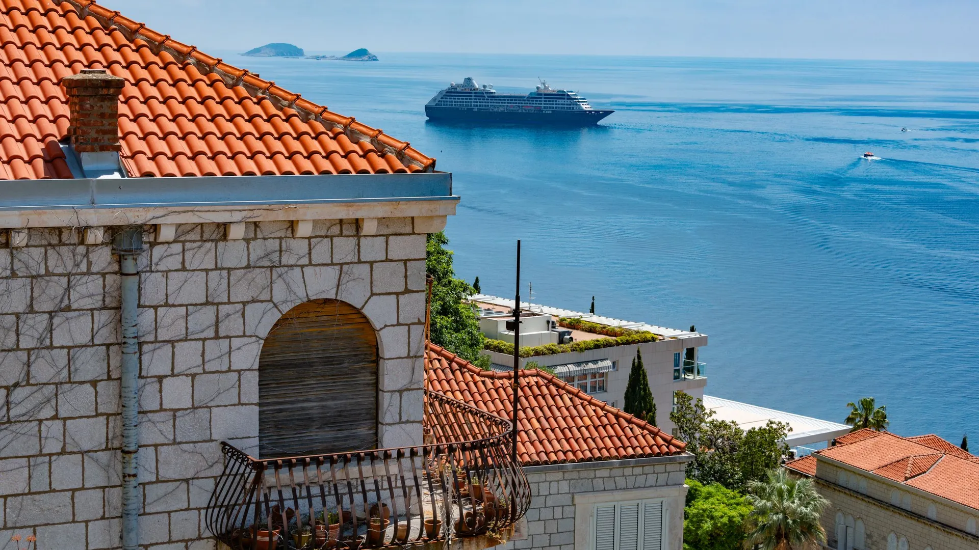 A cruise ship lying at anchor offshore beyond the red-tiled rooftops of Dubrovnik