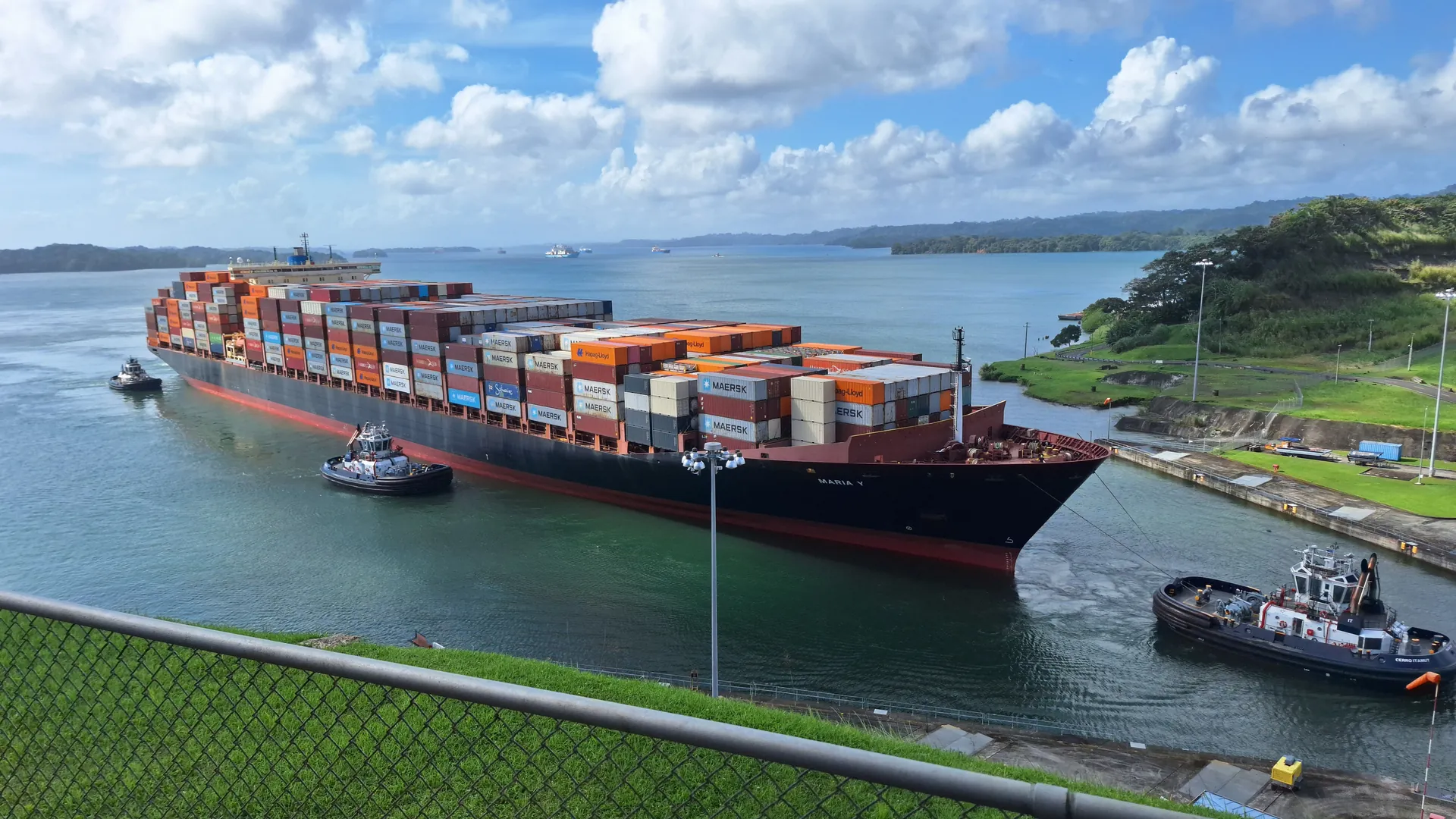 A large container ship guided by tugboats through a lock in the Panama Canal