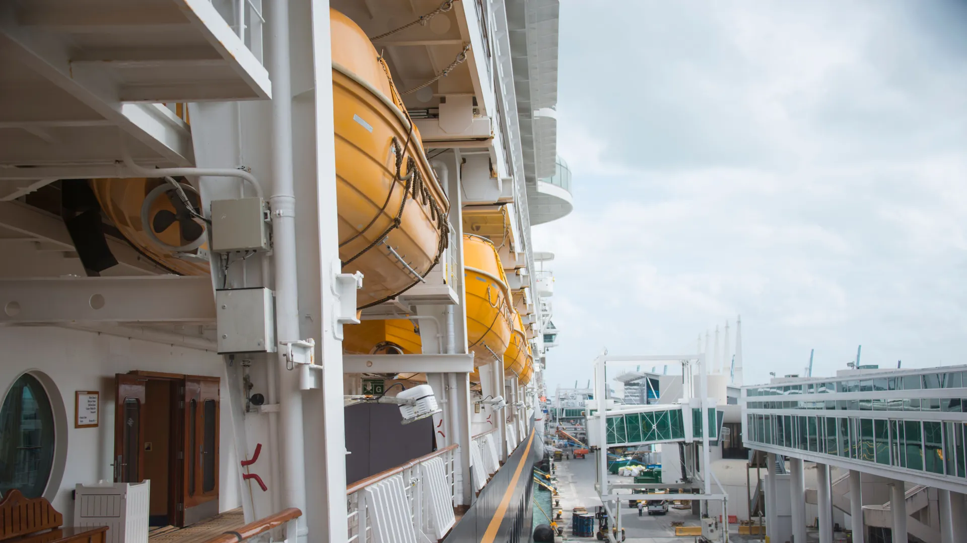 A row of lifeboats along the side of a cruise ship docked in port