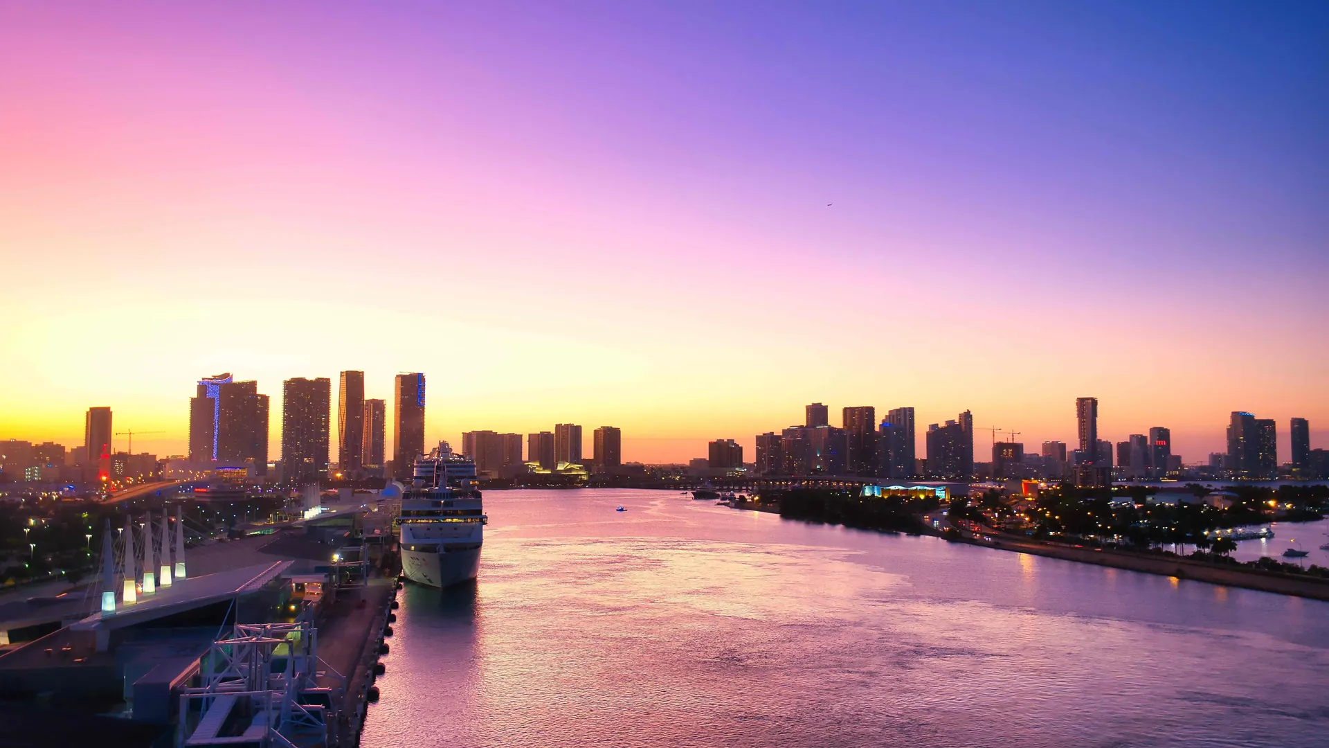A cruise ship docked at PortMiami at sunset, with the downtown Miami skyline across the water