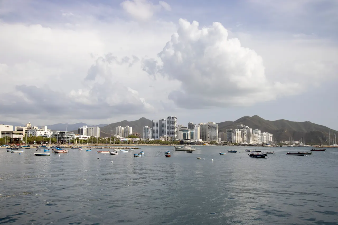 A scenic view of Santa Marta harbor with boats and a city skyline against mountainous backdrop.