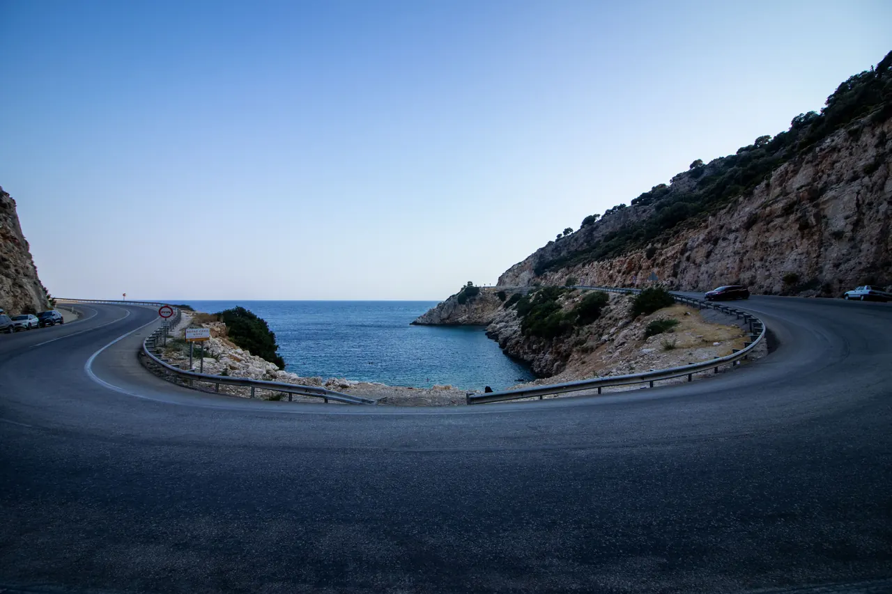 A scenic coastal road with a dramatic hairpin turn overlooks the deep blue sea at sunset.