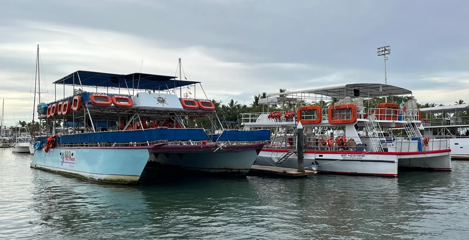 Open-air tour catamarans moored at Puerto Vallarta under a soft grey sky, life rings along their rails