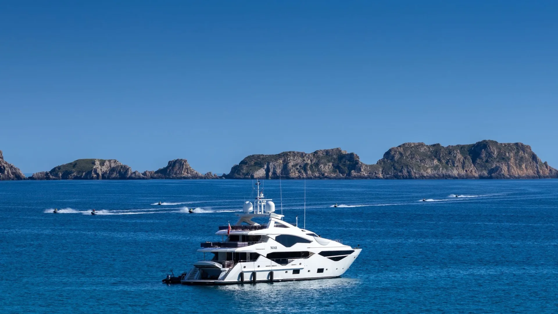 A luxury motor yacht at anchor in deep blue water off a rocky island coastline