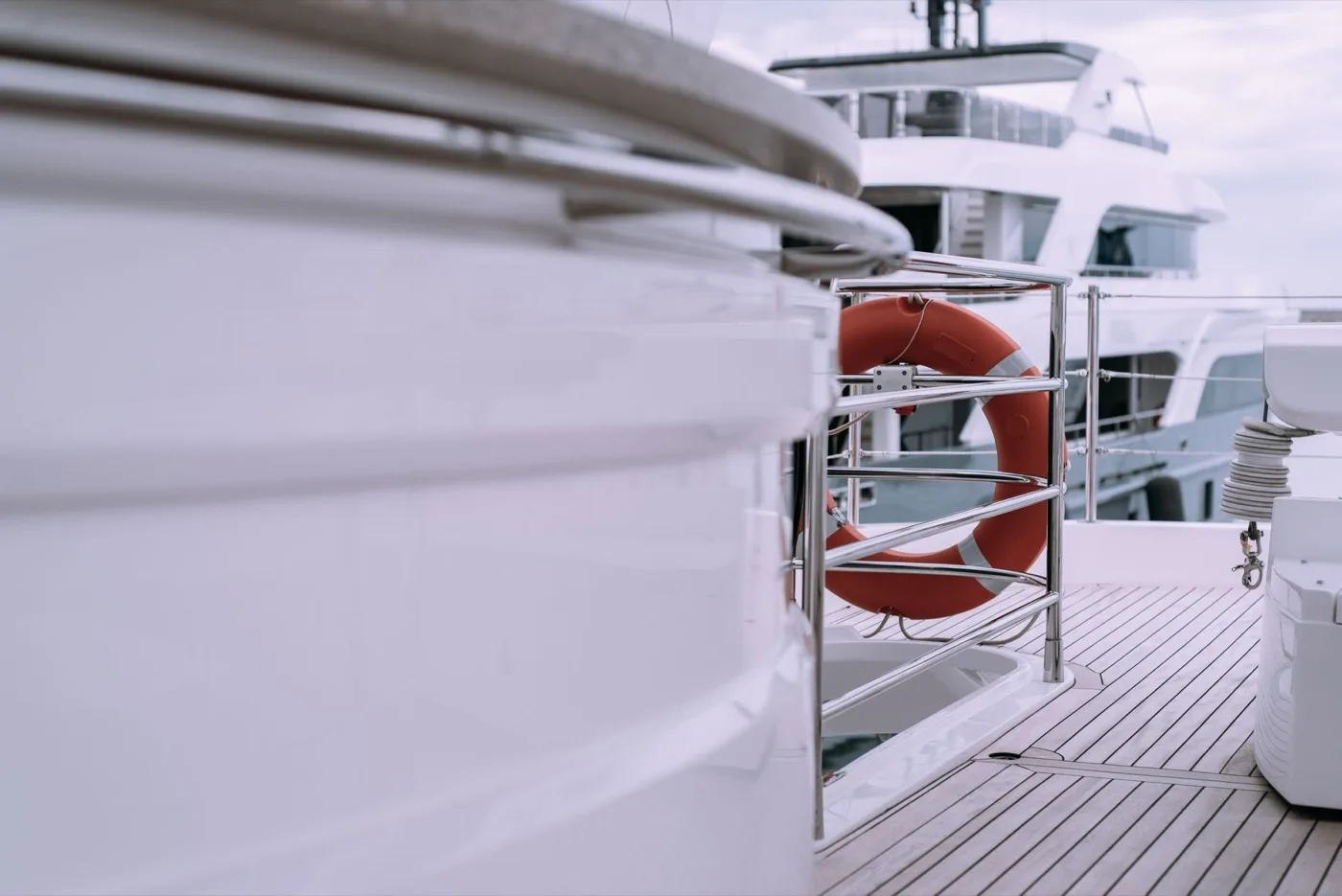 A yacht deck detail with a lifebuoy mounted on white railings above the water