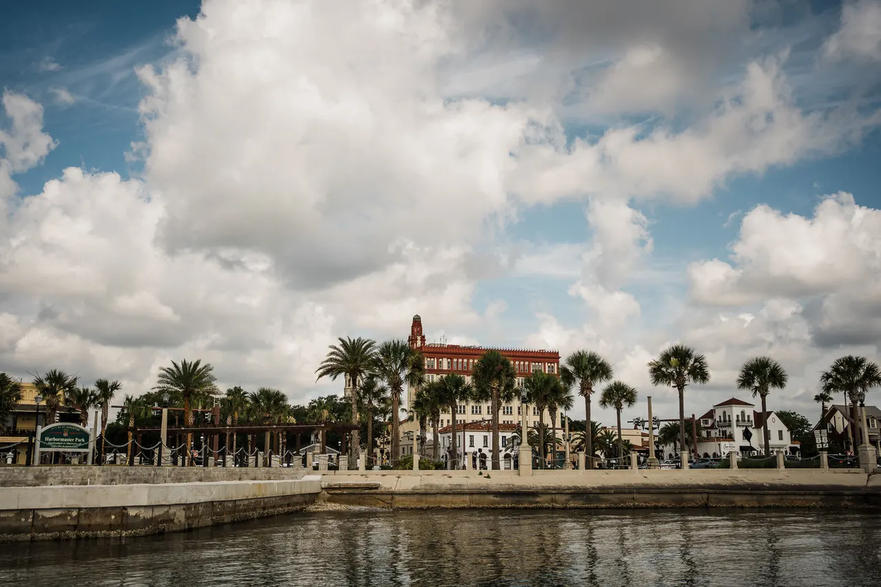 Picturesque view of St. Augustine waterfront with palm trees and historic architecture under cloudy skies.