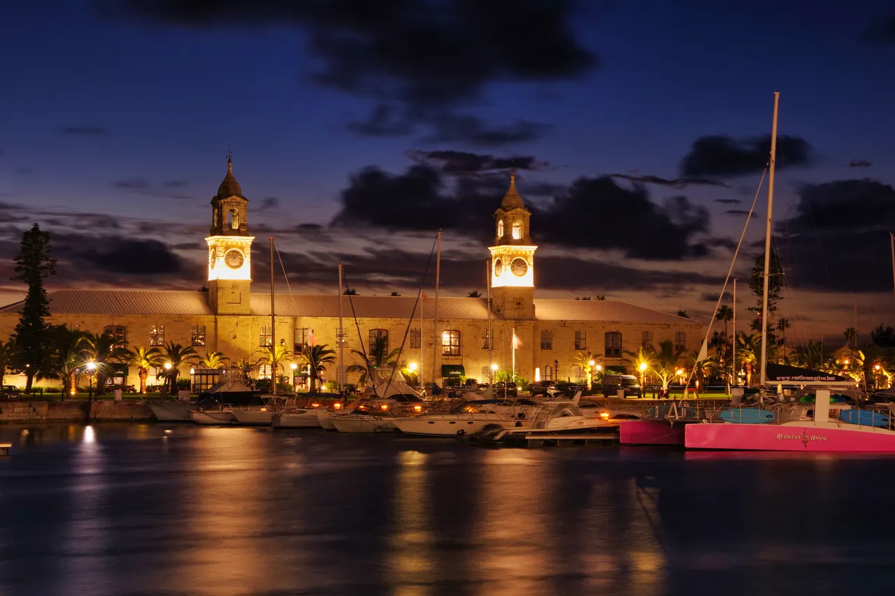 A stunning nighttime view of the Royal Navy Shipyard in Bermuda with illuminated clock towers and yachts.