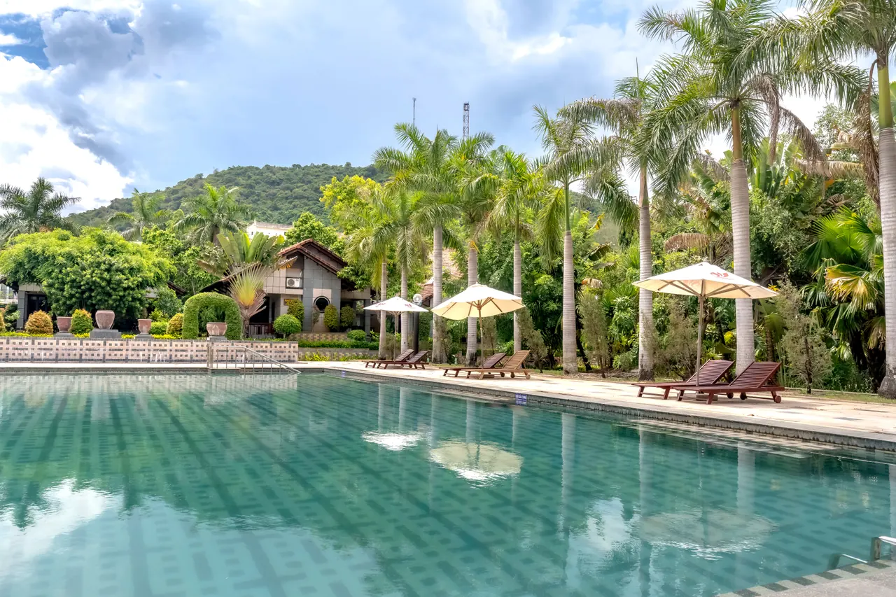 Serene tropical poolside setting with palm trees and loungers under umbrellas.