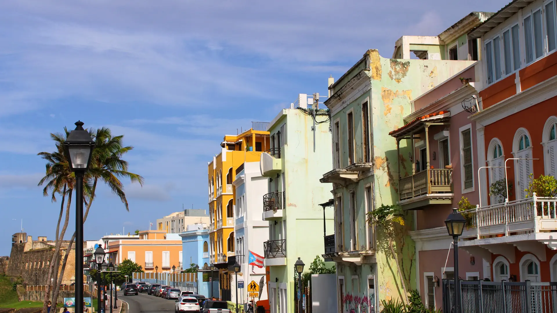 A sunny street in Old San Juan lined with pastel colonial buildings, wrought-iron balconies and a tall palm tree