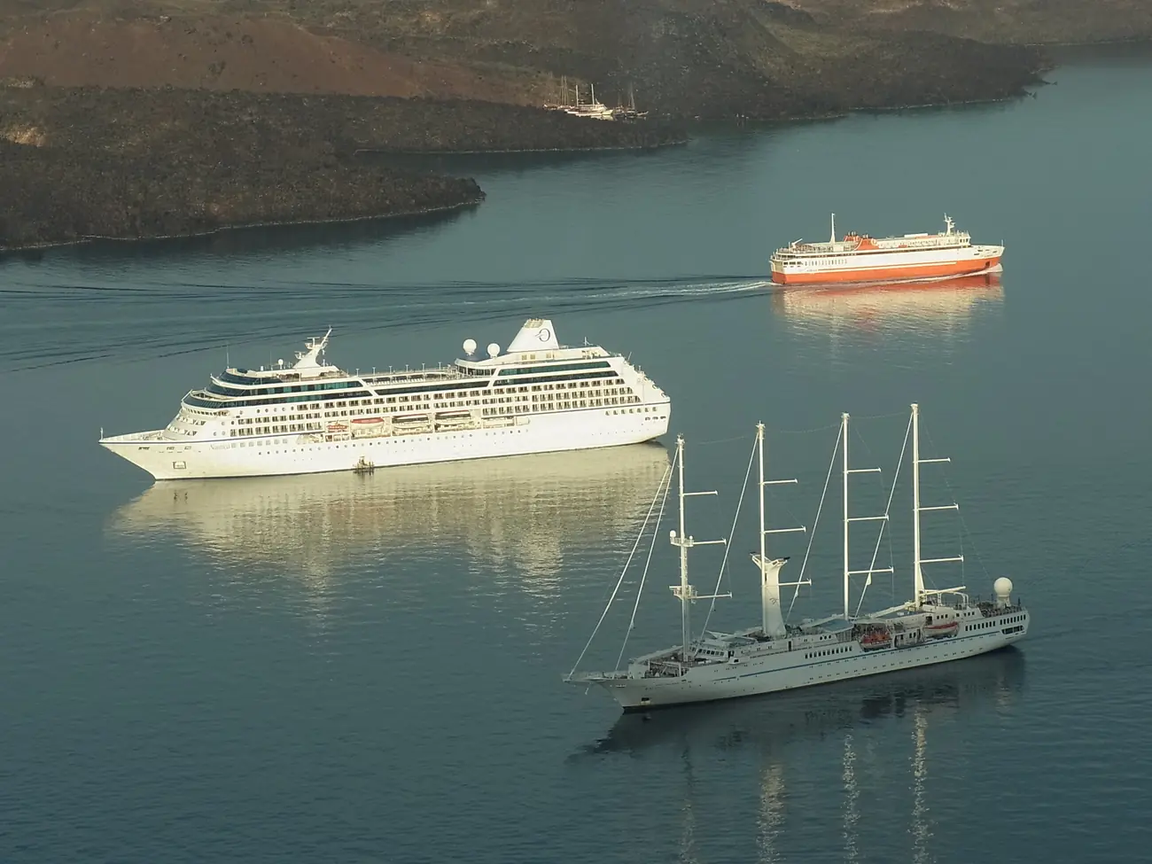 Several cruise ships anchored together in the flooded caldera at Santorini, seen from the cliff above