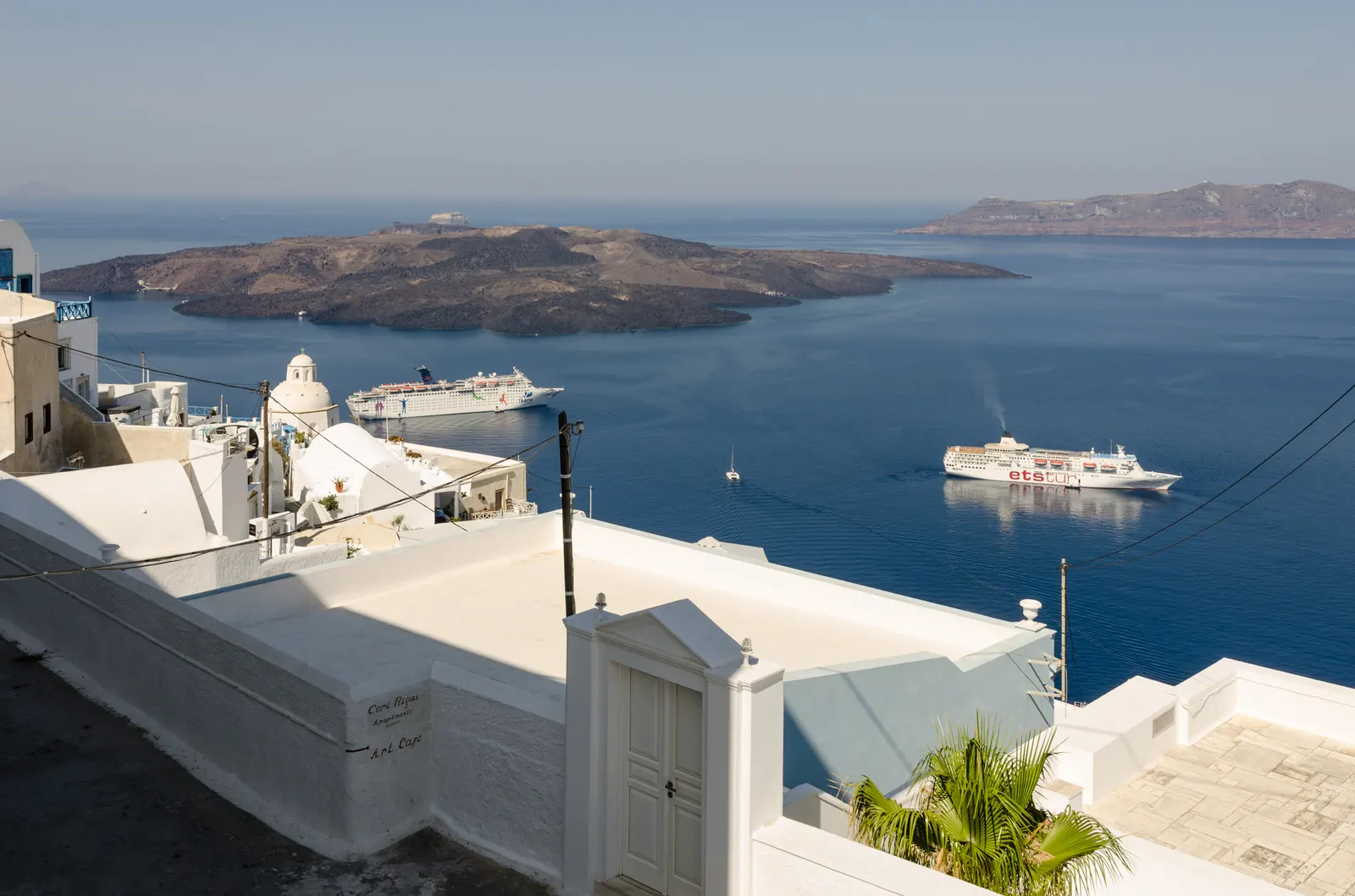 Fira on its caldera cliff above the water at Santorini, with a cruise ship at anchor below and Nea Kameni beyond