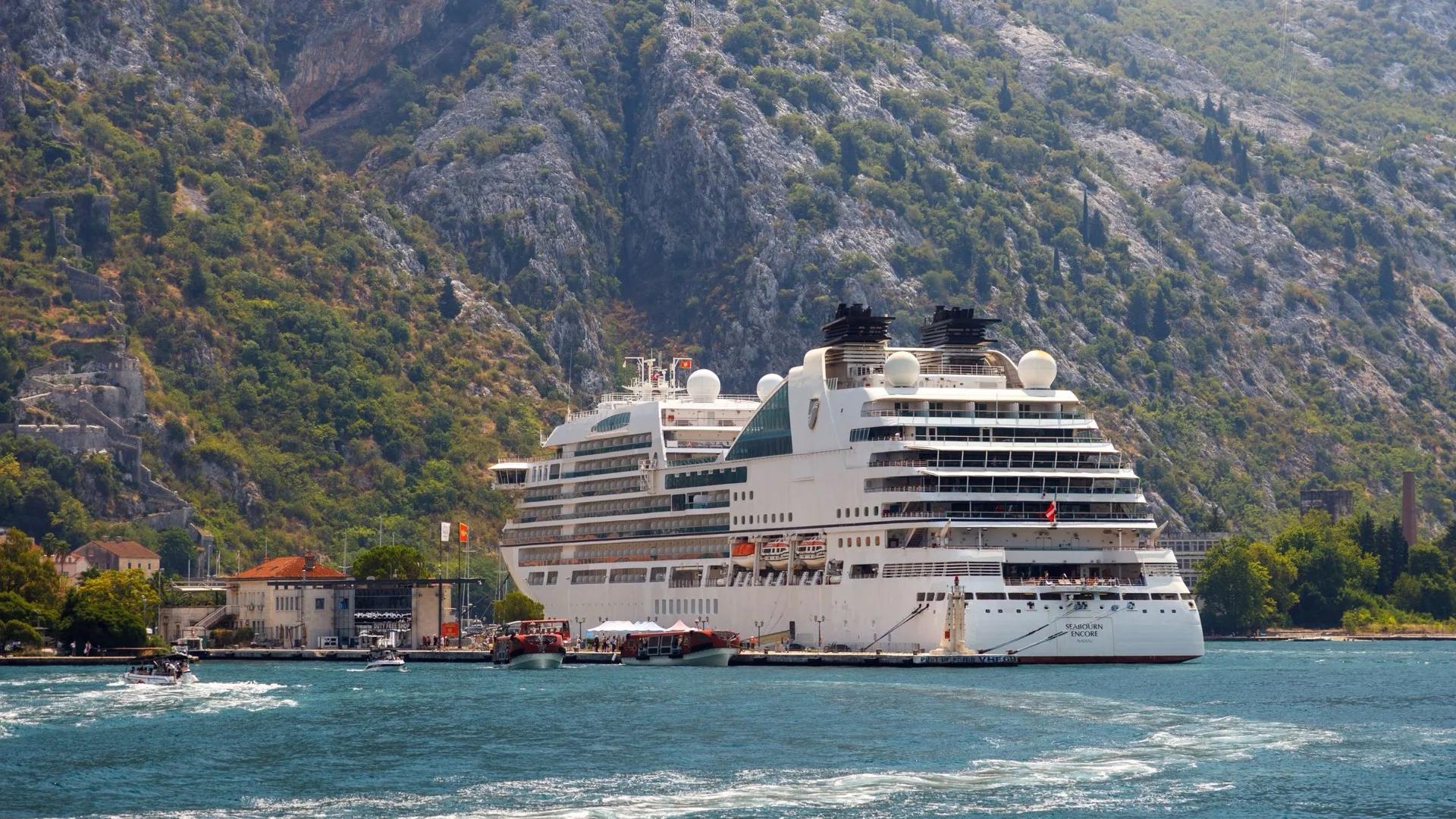 A small luxury cruise ship berthed below steep mountains in a Mediterranean bay