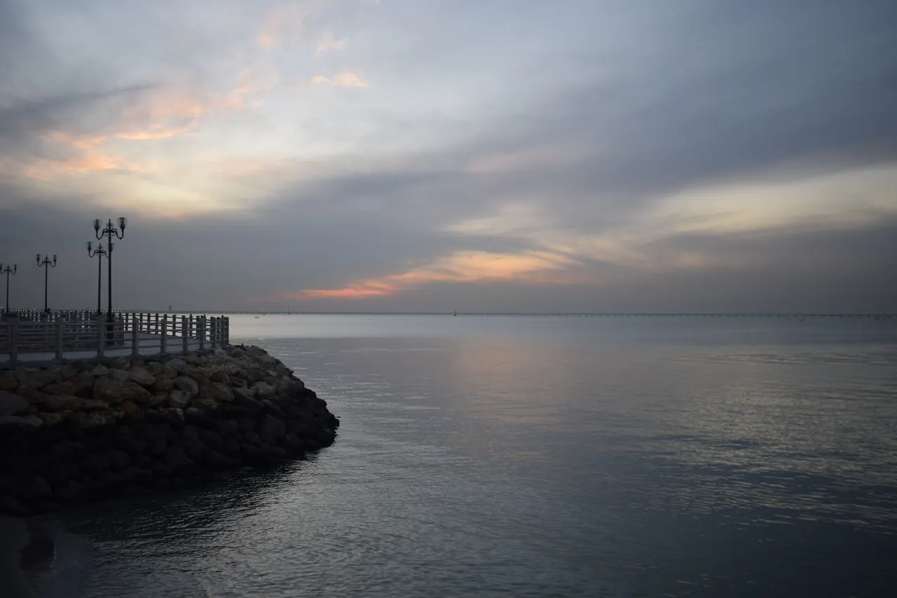 Peaceful view of a rocky shore and promenade during a vibrant sunset.