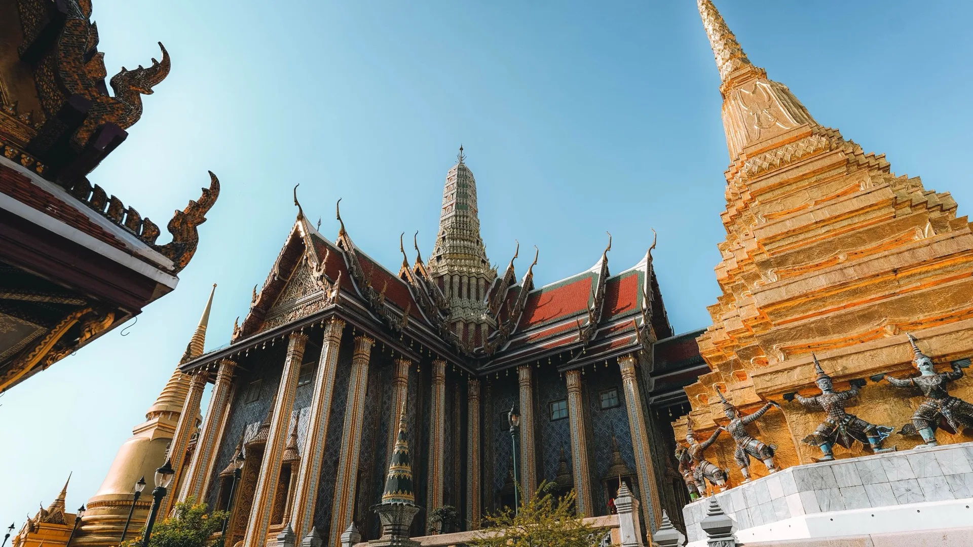 Gilded spires and ornate rooflines of the Grand Palace temple complex in Bangkok against a clear sky