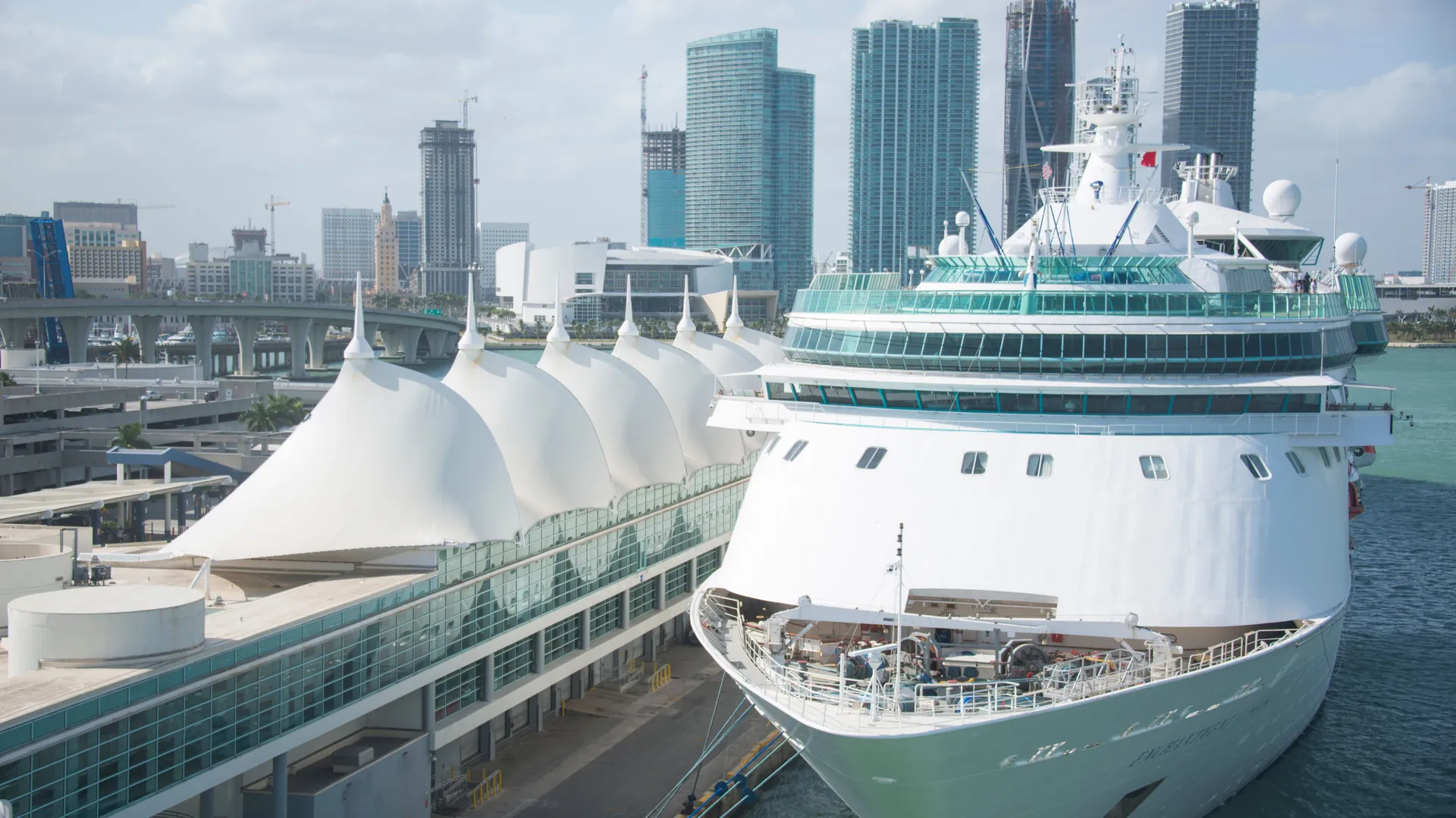 A cruise ship alongside a Miami terminal with downtown towers in the background