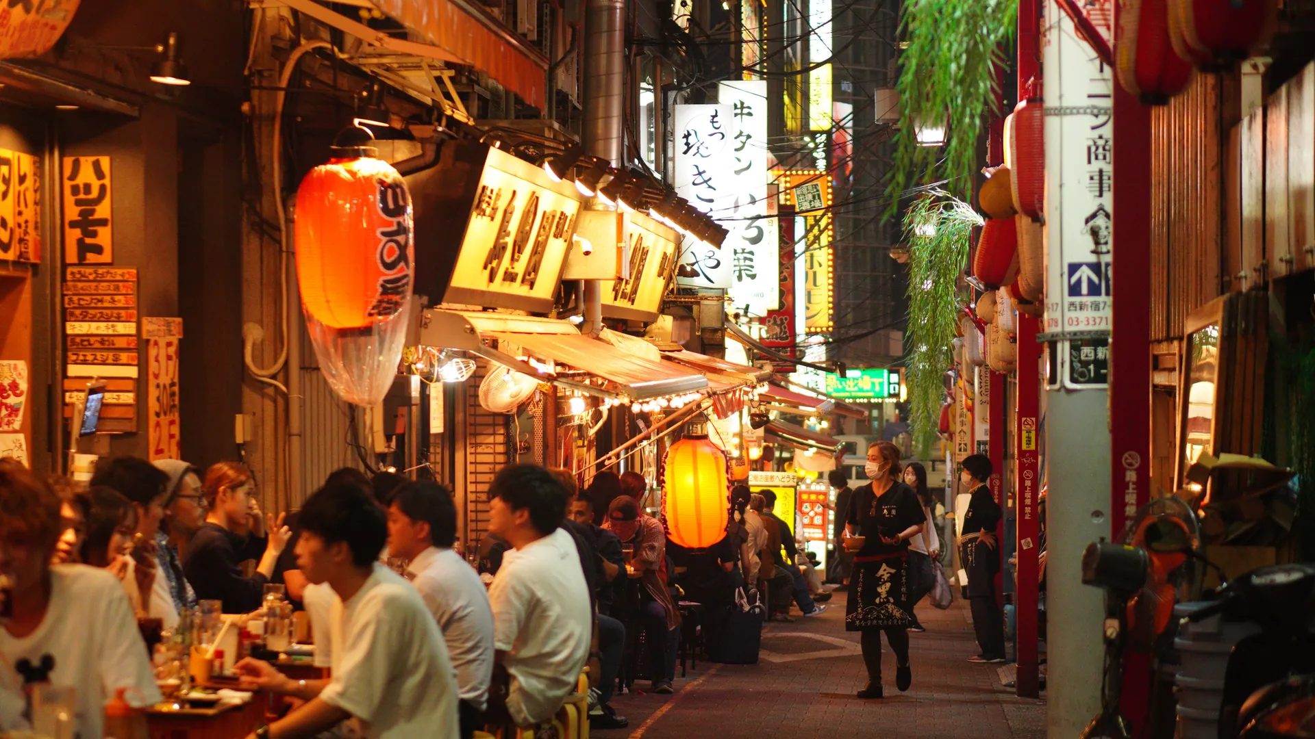 People dining at night in a narrow, lantern-lit alley in Shinjuku, Tokyo