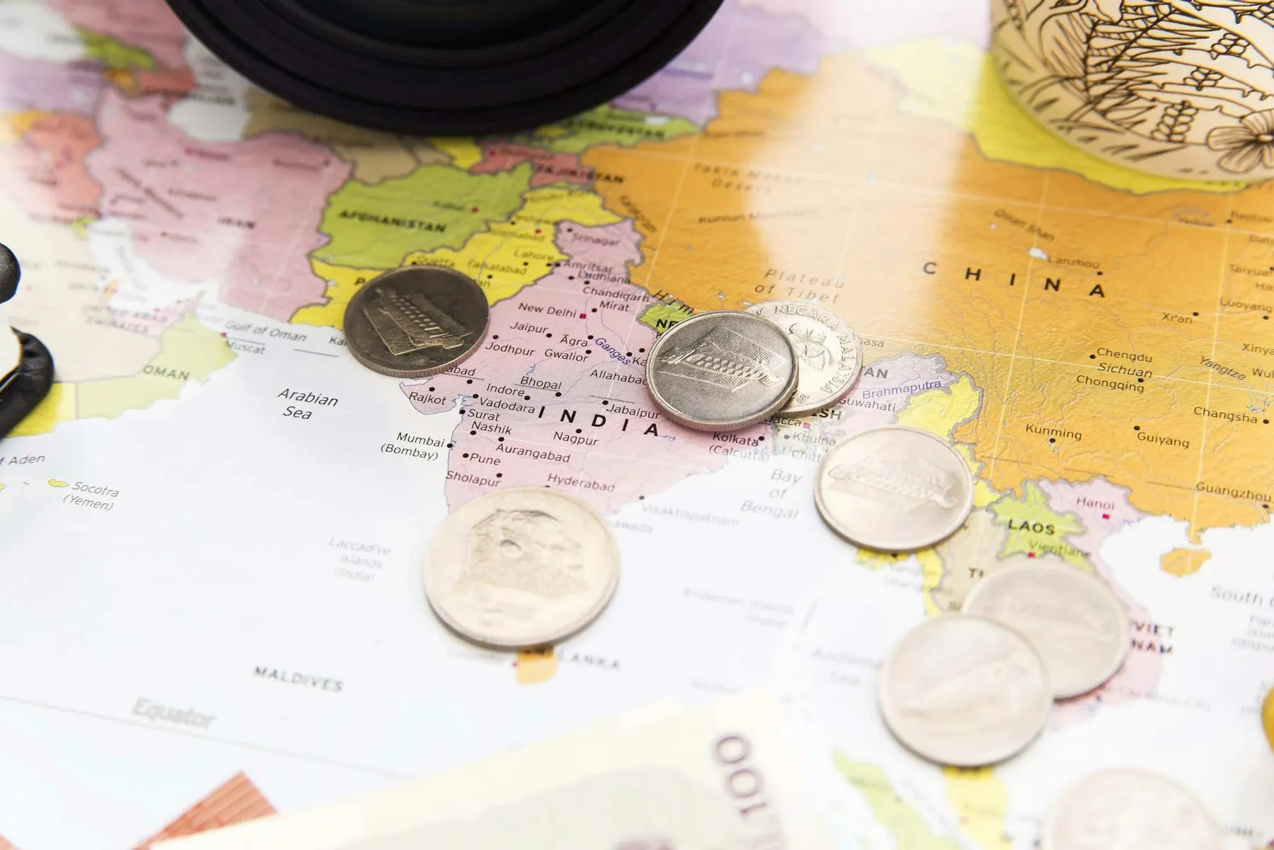 Foreign coins and banknotes scattered across a world map — exchange rates shaping where to travel in 2026