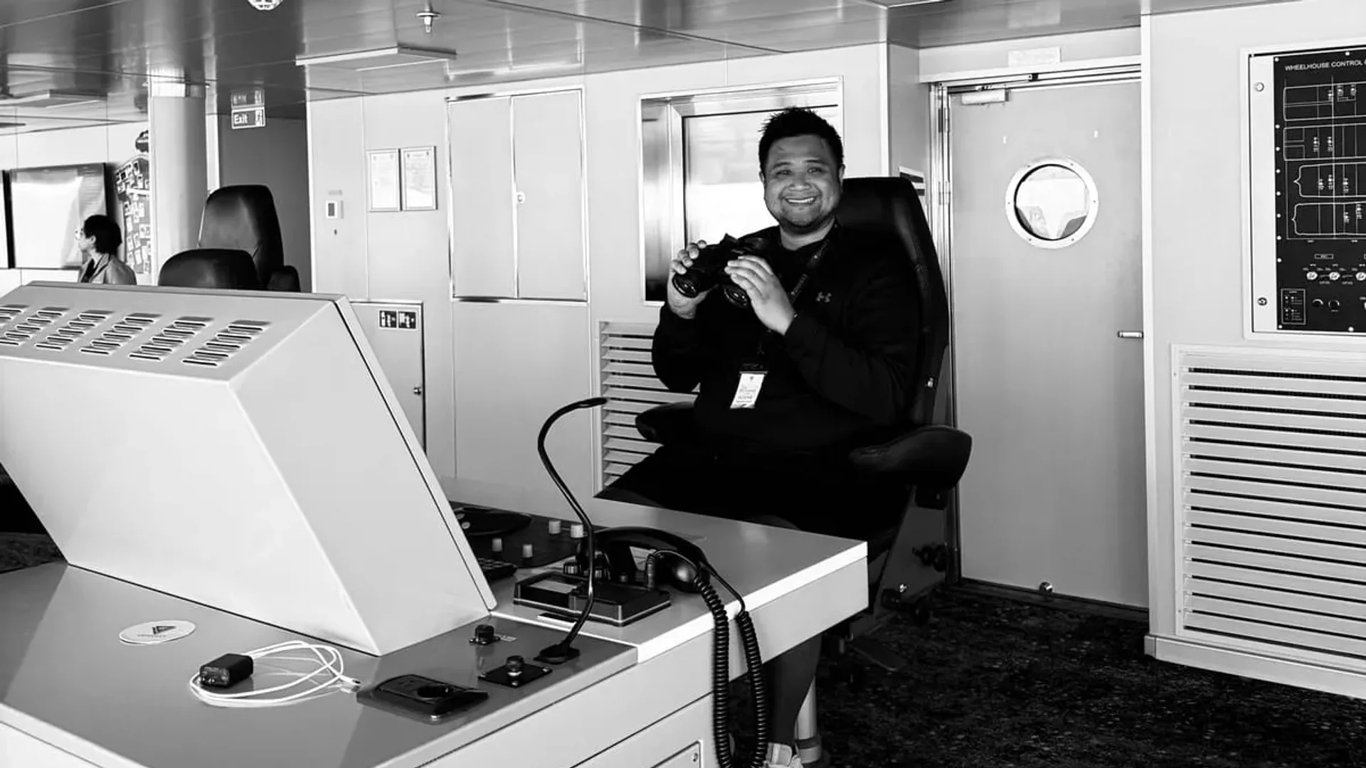 Paolo Melendez on a ship's bridge, holding binoculars beside the wheelhouse console