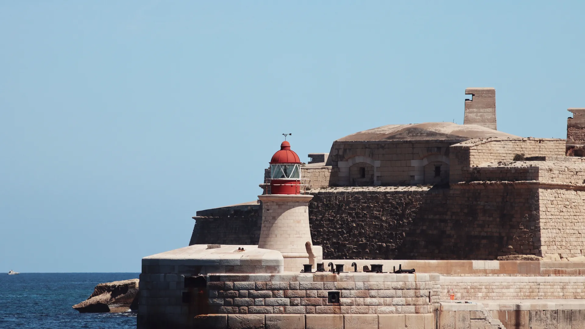 A lighthouse standing beside old stone fortifications at the edge of the sea