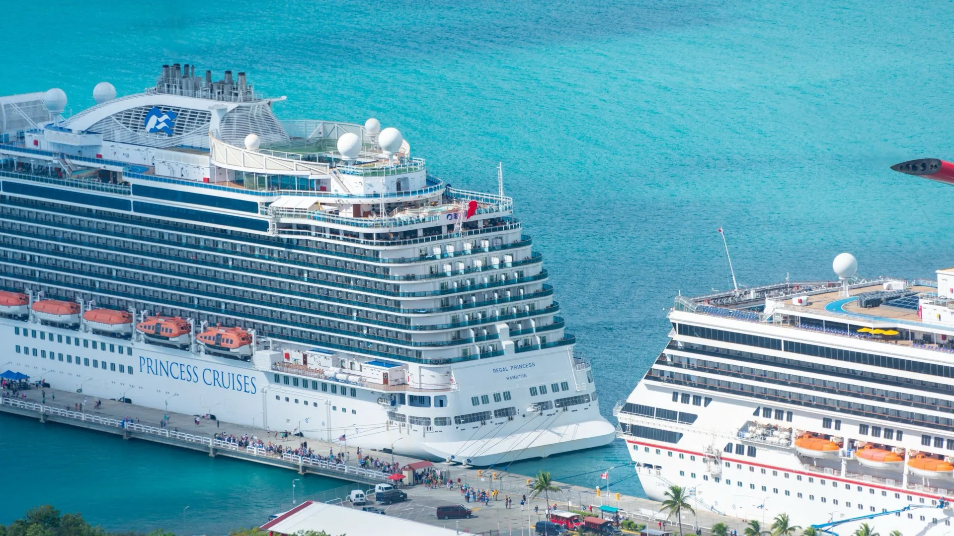 Two cruise ships alongside a pier in clear turquoise Caribbean water, seen from above