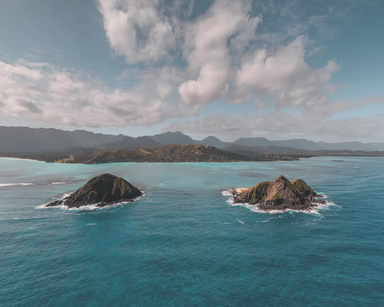 Aerial view of Moku Nui and Moku Iki islands surrounded by turquoise ocean waters near lush coastline.